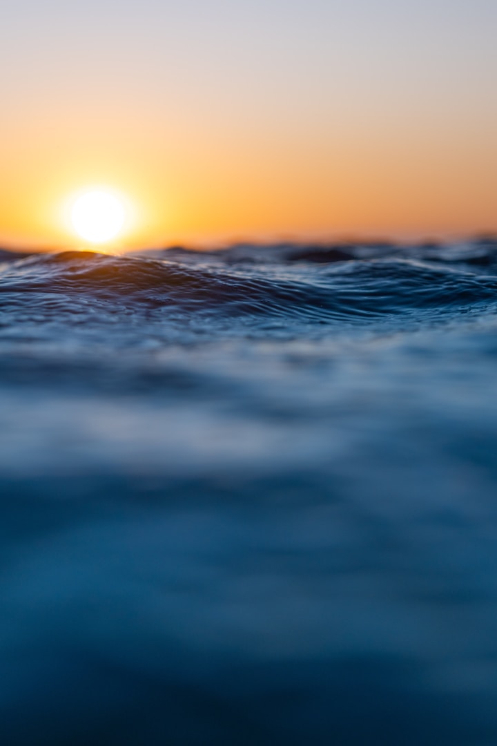 Sonnenuntergang über ruhigem Wasser mit sanften Wellen und orangefarbener Helligkeit.